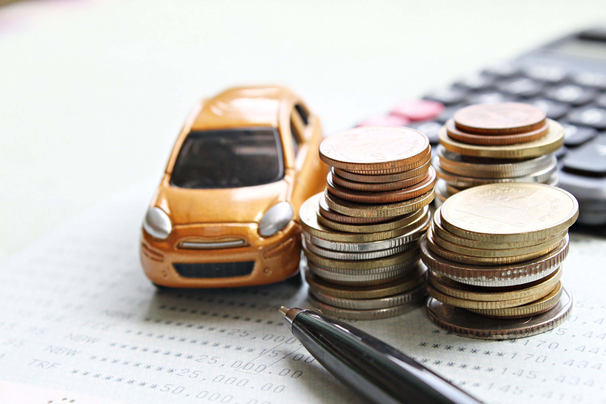 Miniature car model, coins stack, calculator and saving account book or financial statement on office desk table